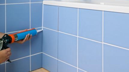 Ръце, нанасящи уплътнител отстрани на ваната